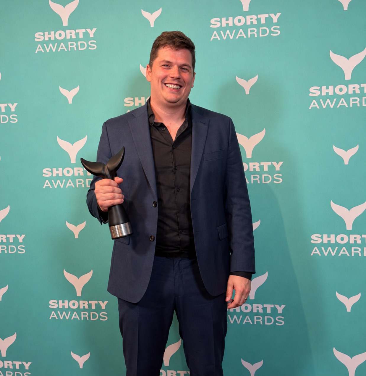 Leroy holding the Shorty Award trophy in front of a Shorty Awards backdrop